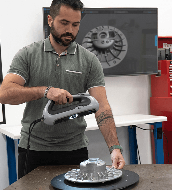 Engineer using a handheld HP DesignScan 3D scanner to scan a mechanical component, visualized on a monitor in the background