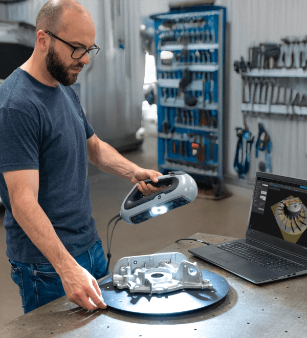 Technician using a handheld HP DesignScan 3D scanner to scan an automotive oil pump, with live scan data visualized on a connected laptop